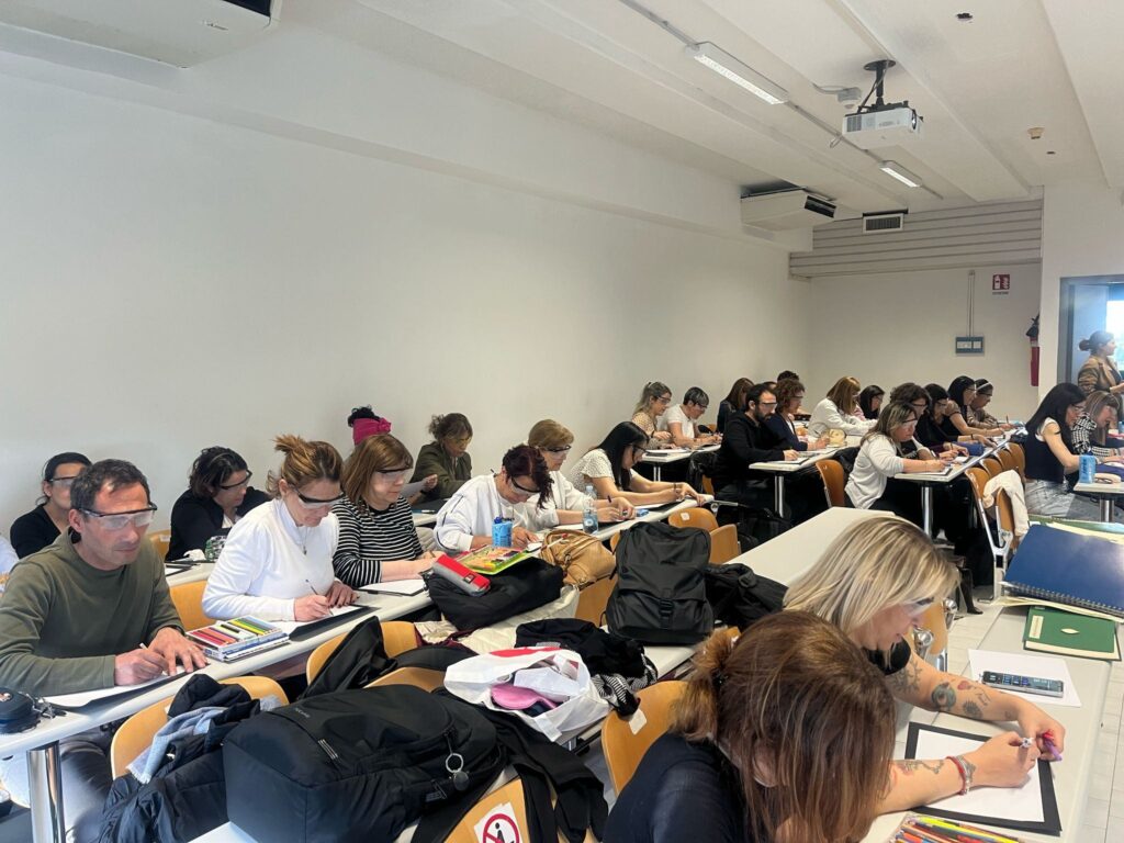 Fotografia di una classe di studenti e docenti seduti al banco durante un momento di Tutti indossano degli occhiali speciali per simulare una perdita di acuità visiva, e tentano di leggere e scrivere.
